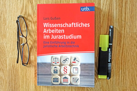 Buch wissenschaftliches Arbeiten im Jurastudium liegt auf dem Tisch, daneben eine Brille und zwei Stifte