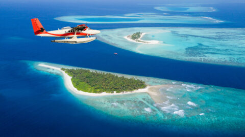 Foto eines Flugzeugs über dem Ozean; im Wasser sind kleine Inseln und die Strukturen des Wassers mit unterschiedlicher Färbung zu sehen