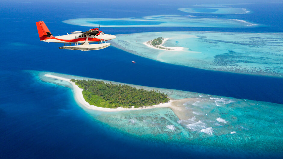 Foto eines kleine Flugzeugs über dem Ozean, in dem kleine Inseln zu sehen sind und unterschiedliche Blauschattierungen des Wassers