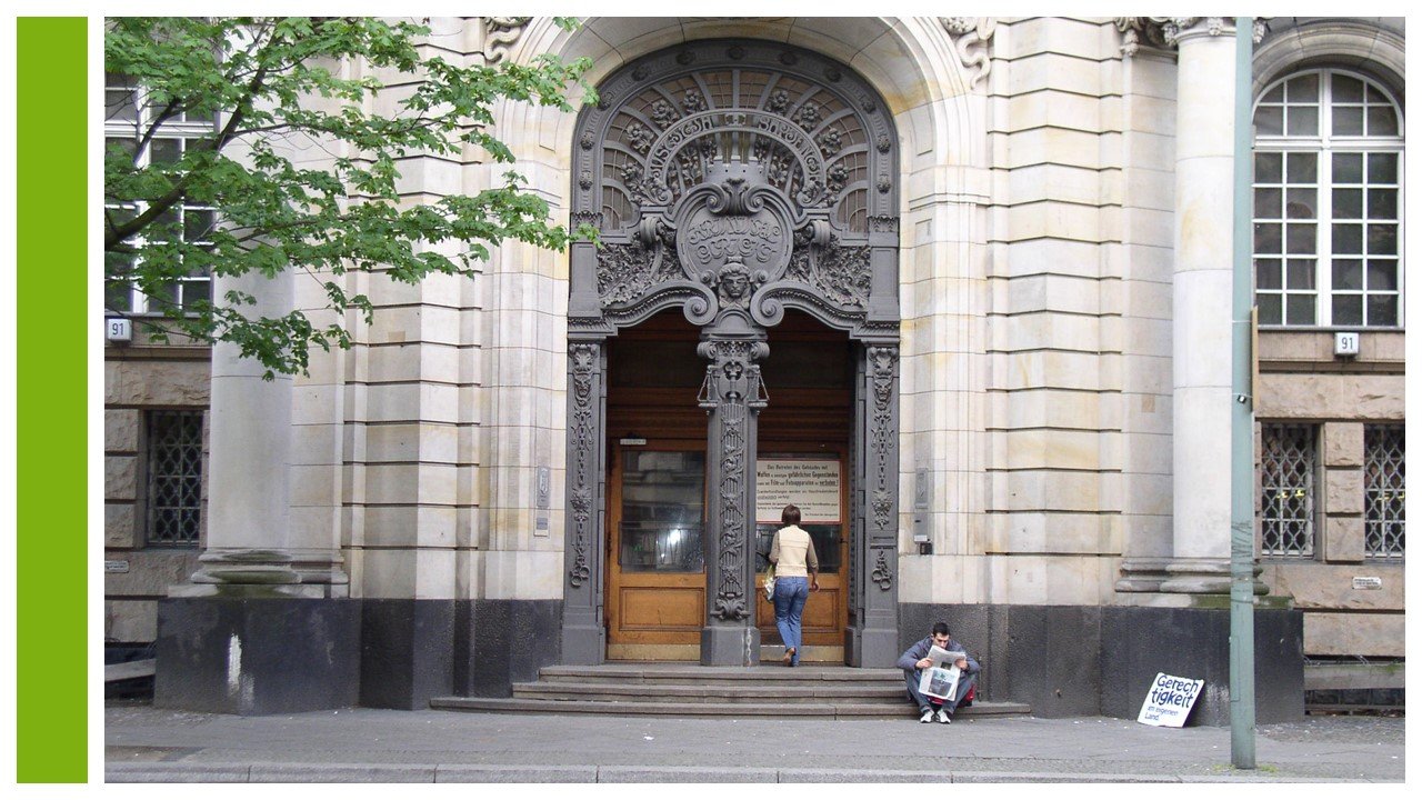 Folie mit einem folienfüllenden Bild des Eingangs vom Kriminalgericht Moabit in Berlin, am linken Rand ein senkrechter grüner Streifen